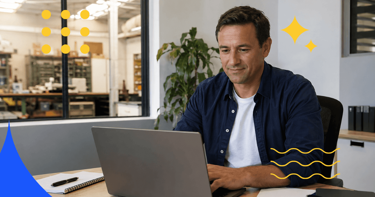 Man working on a laptop in an office next to a factory floor